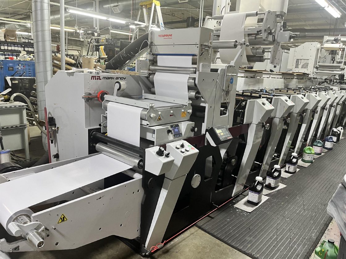 A Mark Andy P7 flexo press line with ink stations running the length of the deck and a corona treatment unit mounted above the web