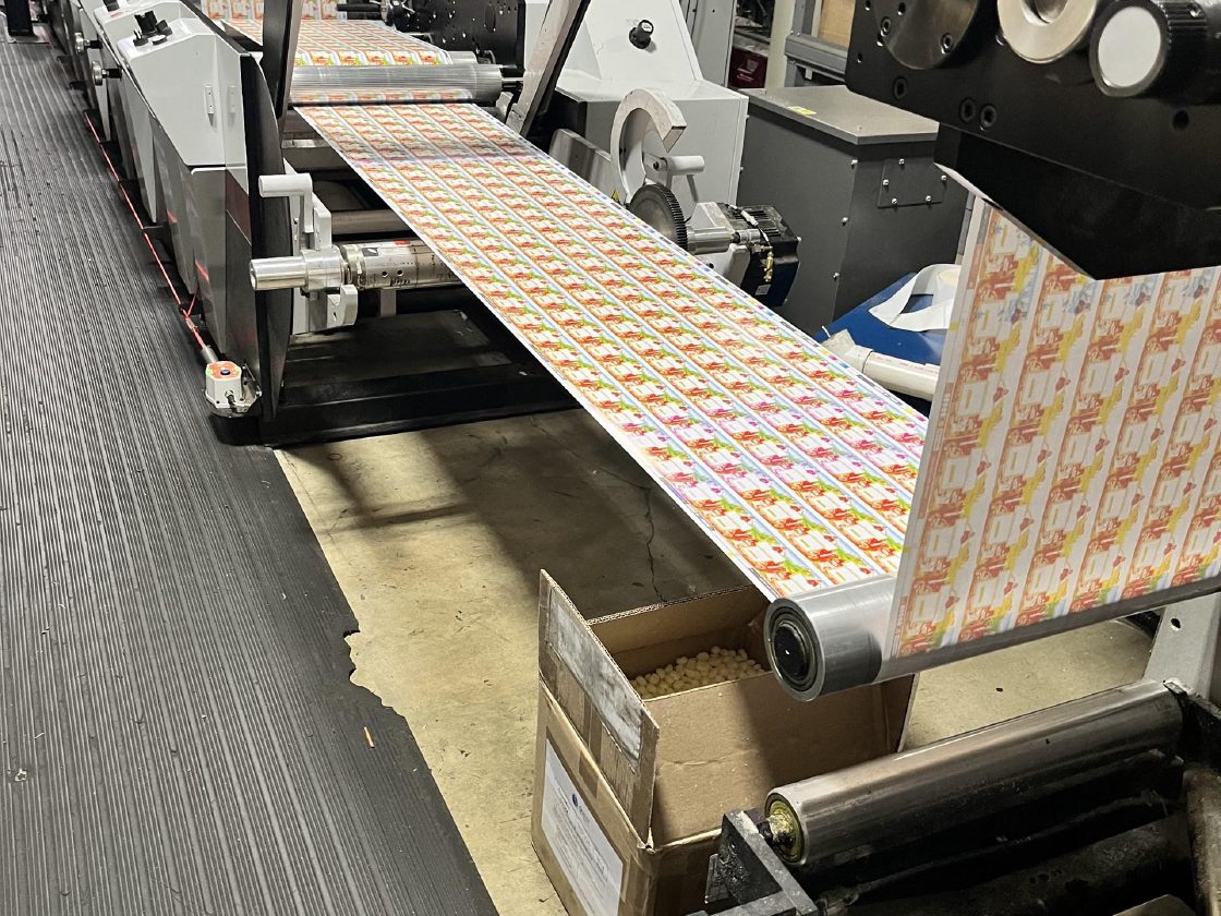 A printed label web running off the press in full color, with a color control bar along the edge of the web