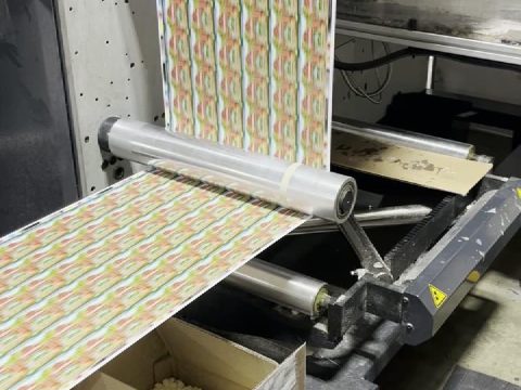 Printed label web running down from the press deck and over a roller, filmed mid-run