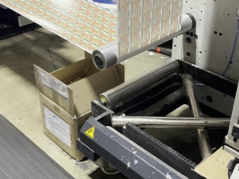 Printed label web travelling across rollers through the back end of the press